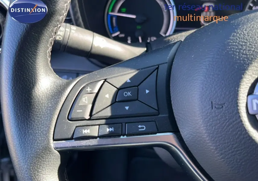 Gros plan sur les commandes au volant côté gauche du Nissan Juke 2024 gris squale métal, avec tableau de bord hybride en arrière-plan.
