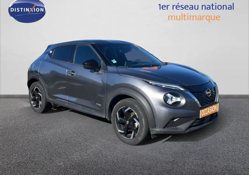 Nissan Juke Hybrid gris squale métal vu en 3/4 avant droit avec jantes noires et toit foncé.
