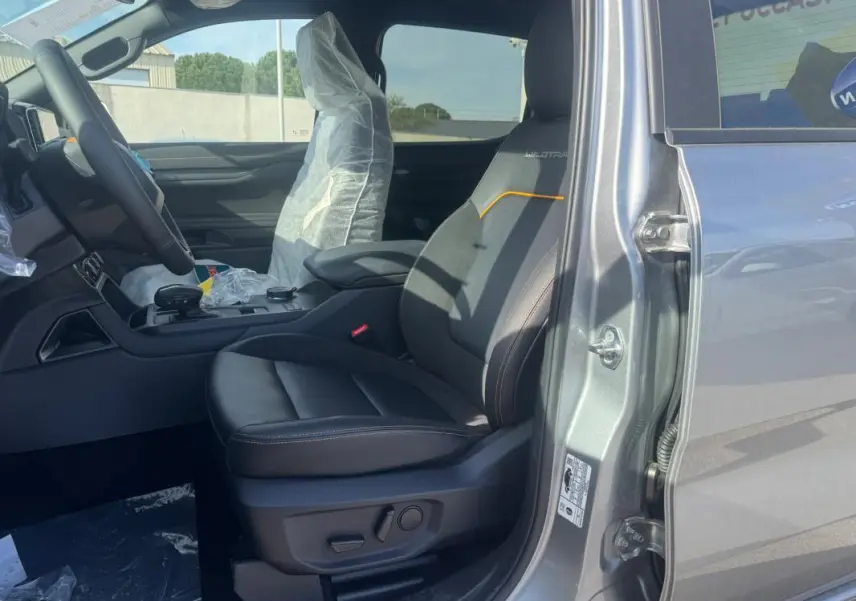 Vue côté droit de l'intérieur gris du Ford Ranger Wildtrak 2025, siège avant en cuir avec surpiqûres orange et accoudoir central.