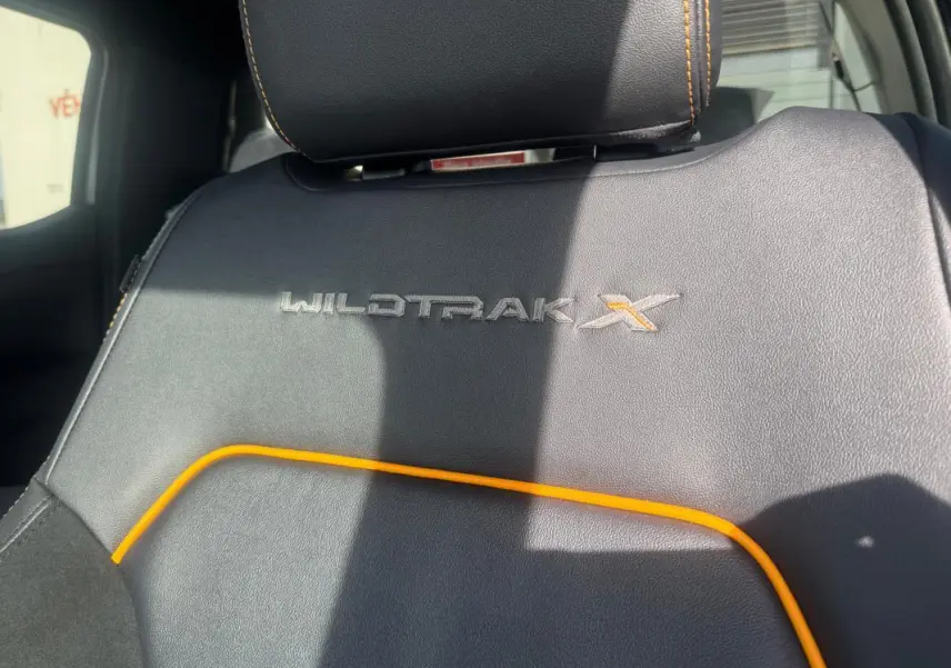 Détail du siège avant en cuir noir avec surpiqûres orange et logo Wildtrak X brodé.