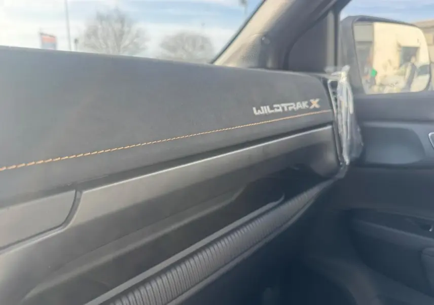 Détail intérieur côté passager du Ford Ranger Wildtrak X 2025 avec tableau de bord noir et surpiqûres orange.