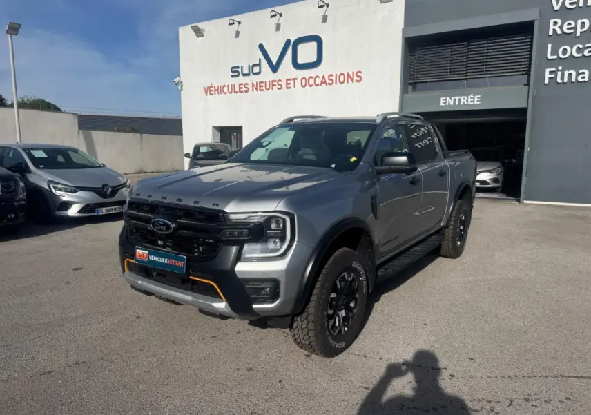 Ford Ranger Wildtrak gris vu en 3/4 avant droit, avec barres de toit et jantes alliage noires.