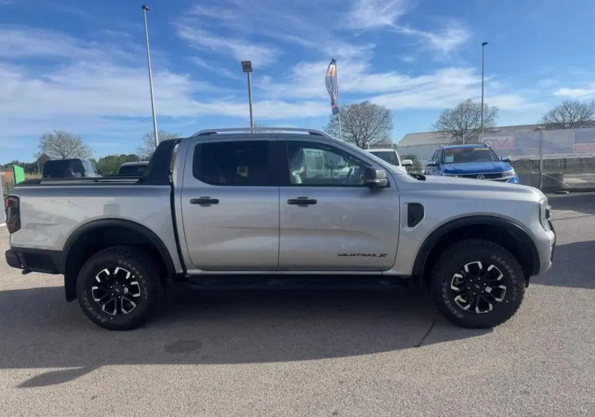 Vue de profil côté gauche du Ford Ranger gris 2025 Wildtrak X avec jantes alliage noires et barres de toit visibles.