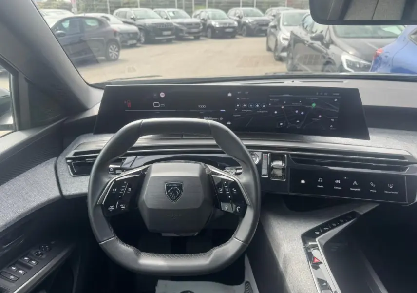 Vue intérieure centrée sur le volant Peugeot et le cockpit numérique large du 5008 noir, avec tableau de bord moderne et écran tactile.