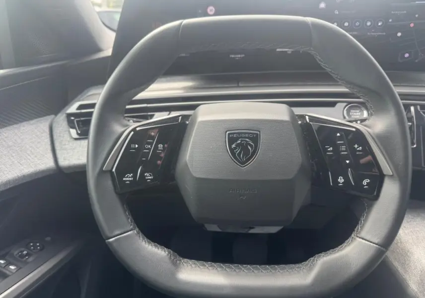 Gros plan sur le volant cuir noir du Peugeot 5008 2025 avec commandes intégrées et logo Peugeot central.