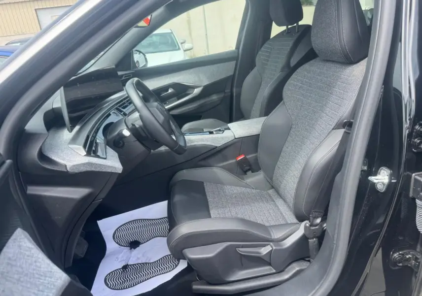 Vue intérieure côté conducteur du Peugeot 5008 noir 2025, sièges tissu et cuir avec tableau de bord moderne.