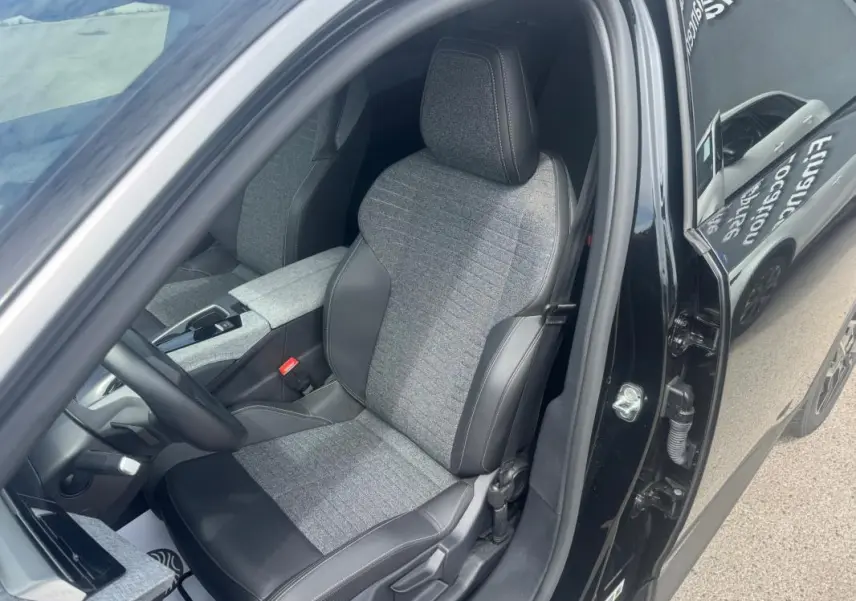 Vue intérieure côté conducteur du Peugeot 5008 noir 2025, mettant en valeur le siège tissu et cuir avec accoudoir central.