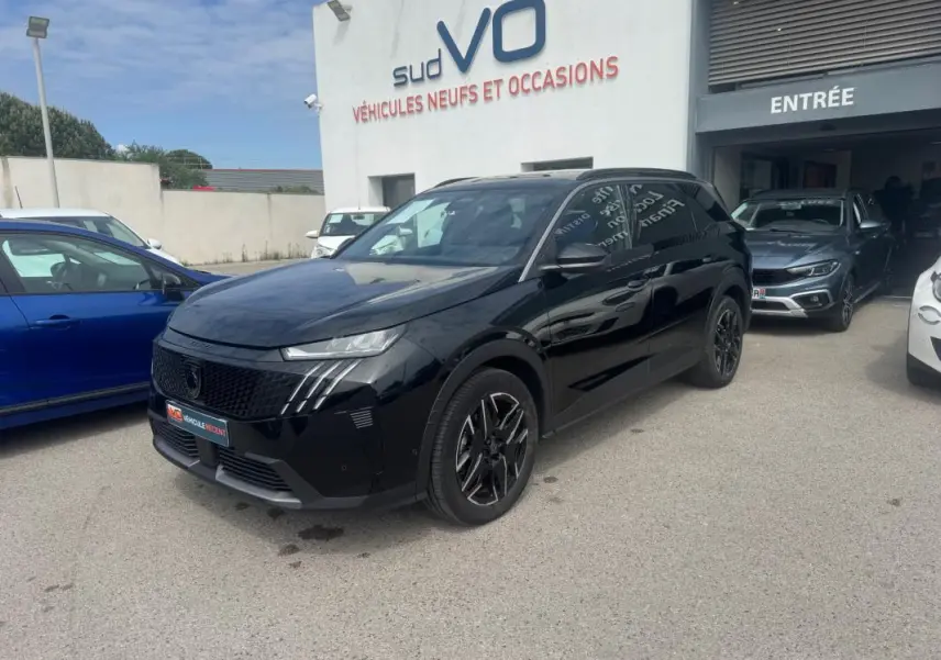 Peugeot 5008 Hybrid noir en 3/4 avant droit, avec jantes alliage noires et barres de toit visibles sur parking.