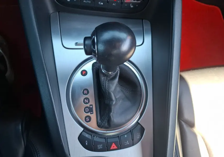Gros plan sur la commande de boîte automatique d’une Audi TT rouge, avec levier en cuir et console alu brossé.