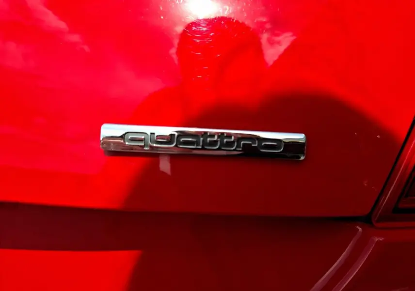 Gros plan sur l’inscription « quattro » chromée à l’arrière d’une Audi TT rouge vif, sous un angle latéral droit.
