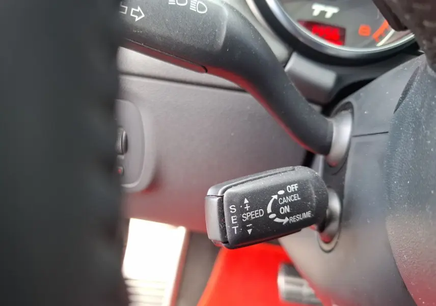 Gros plan sur le levier de régulateur de vitesse de l'Audi TT rouge, visible derrière le volant côté gauche.