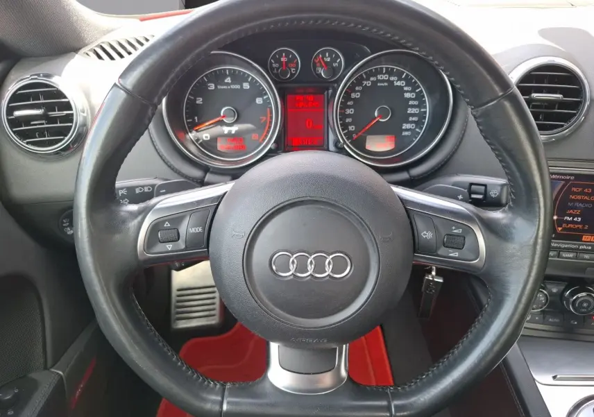 Vue centrée sur le volant en cuir noir d'une Audi TT 3.2 V6 Quattro 2007 avec palettes au volant et tableau de bord rouge.