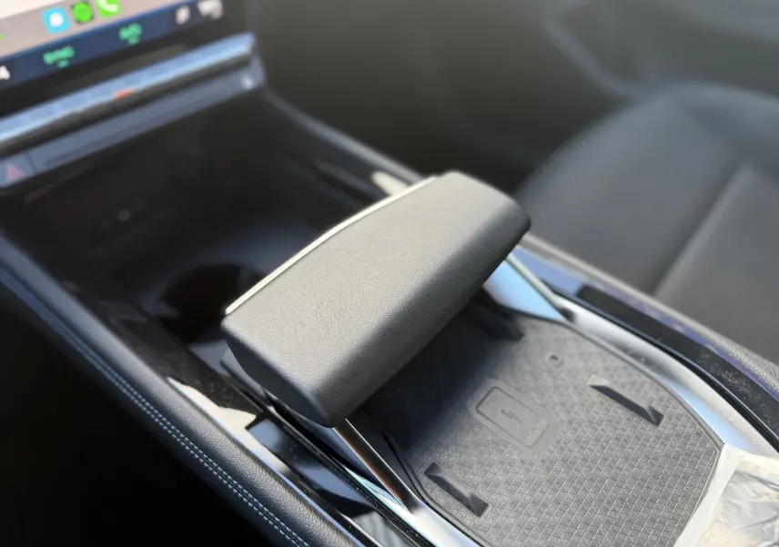 Gros plan sur la console centrale noire du Renault Austral Hybrid 2025, mettant en valeur le repose-bras et le chargeur sans fil.