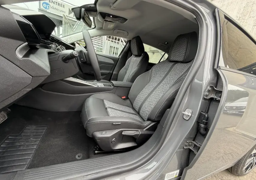 Vue intérieure côté conducteur de la Peugeot 308 gris sellenium, montrant les sièges en tissu et cuir avec surpiqûres contrastées.