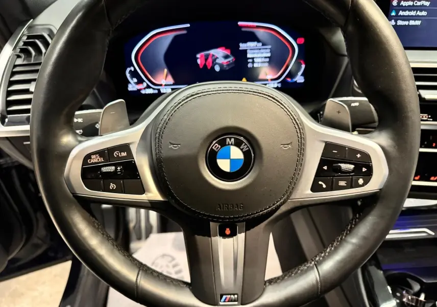 Vue rapprochée du volant cuir noir BMW X4 XDrive 20d 2020 avec commandes intégrées et tableau de bord numérique.