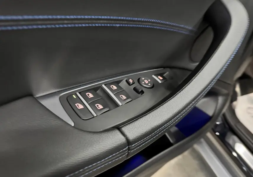 Gros plan sur la commande des vitres côté conducteur en cuir noir avec surpiqûres bleues dans une BMW X4 Carbonschwarz 2020.