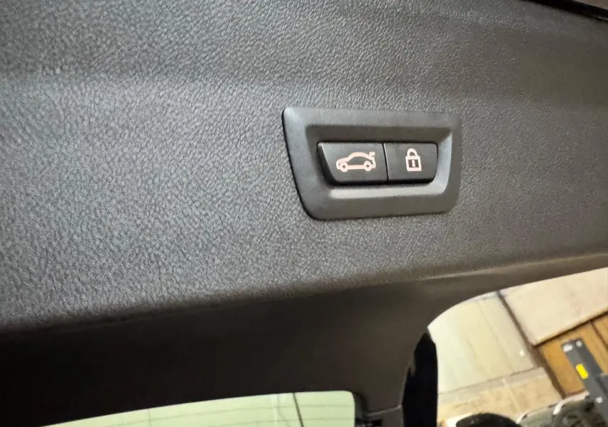 Gros plan sur le bouton d'ouverture et verrouillage du coffre, intérieur noir du BMW X4 XDrive 20d 2020.