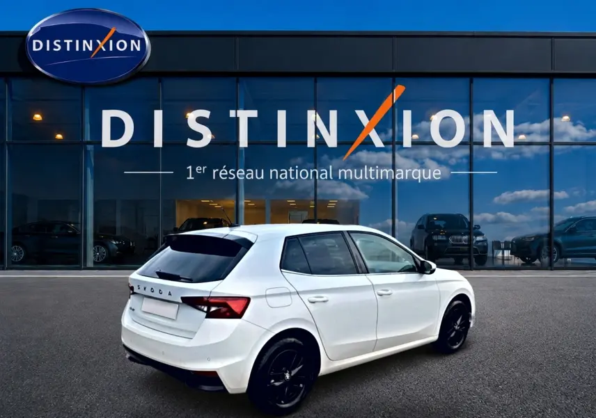 Vue 3/4 arrière droite d'une Skoda Fabia blanche 2025 avec jantes noires, stationnée devant une vitrine Distinxion.