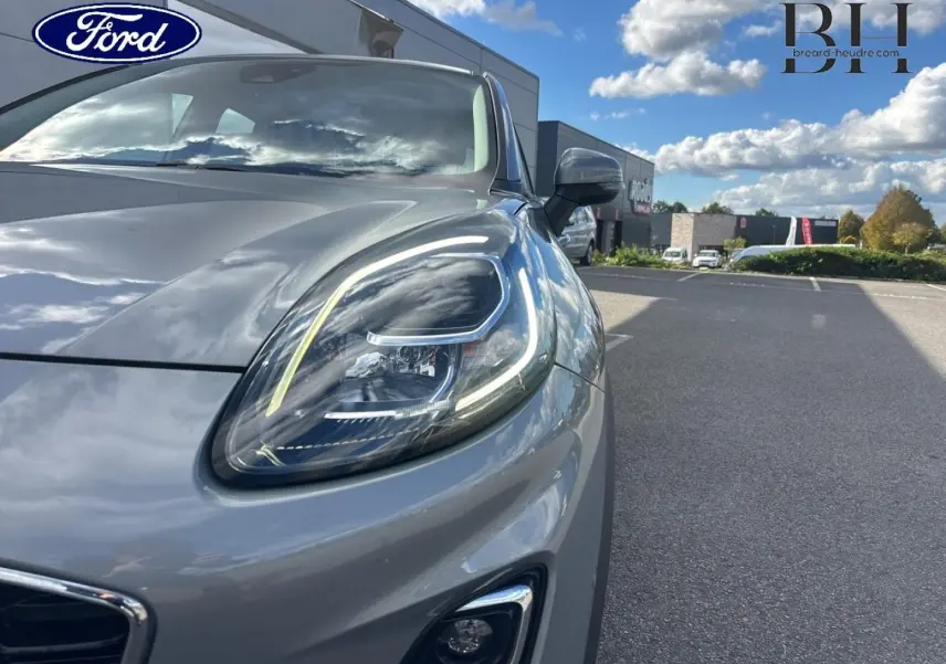 Gros plan sur le phare avant droit du Ford Puma gris Solar métallisé sous un ciel partiellement nuageux.