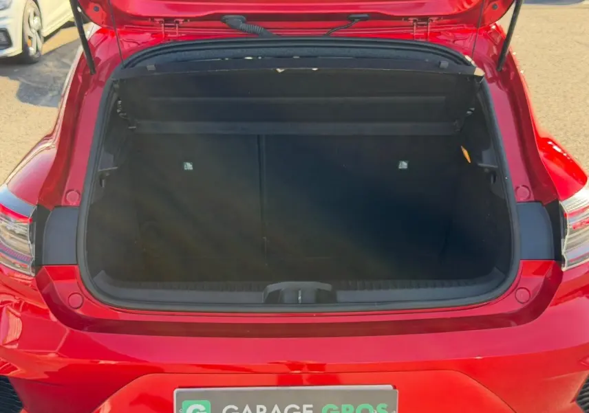 Coffre ouvert vu de l'arrière d'une Renault Clio rouge, montrant l'espace de chargement vide.