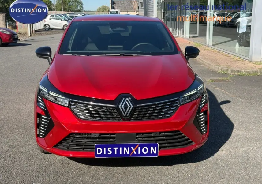 Vue avant d'une Renault Clio rouge avec calandre noire et phares LED, stationnée devant un bâtiment vitré.