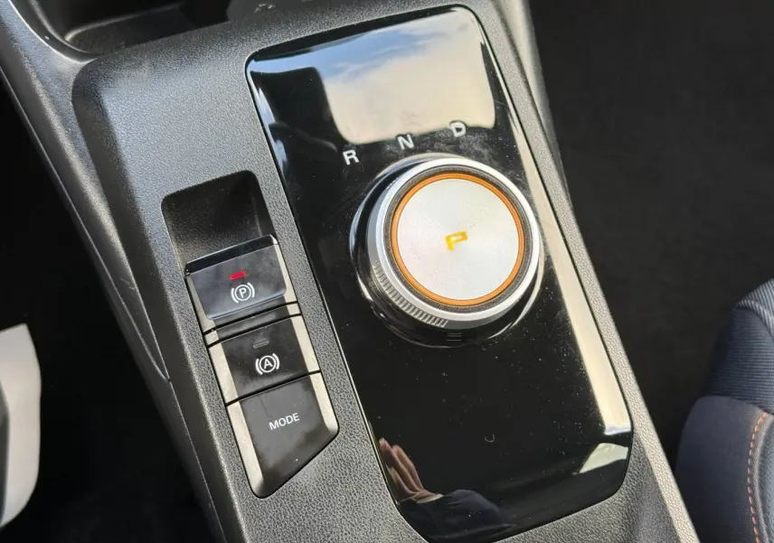 Gros plan sur la console centrale noire du MG3 blanc 2025, avec sélecteur rotatif de boîte auto et boutons de frein à main électronique.