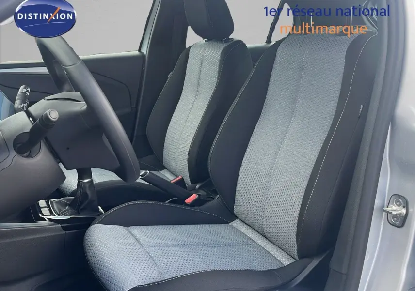 Vue intérieure côté conducteur de l'Opel Corsa 2025 avec sièges tissu gris clair et noir, volant et levier de vitesse manuelle visibles.