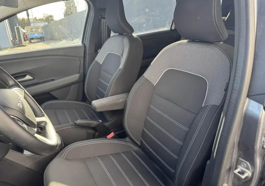 Vue intérieure côté conducteur du Dacia Jogger gris schiste, mettant en valeur les sièges avant en tissu noir avec surpiqûres blanches.