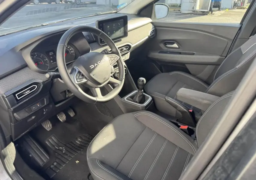 Vue intérieure côté conducteur du Dacia Jogger 2025, montrant le volant, la console centrale et les sièges noirs.