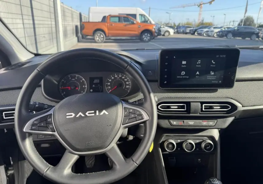 Vue intérieure centrée sur le volant DACIA et l’écran tactile 8 pouces du tableau de bord, ambiance noire.