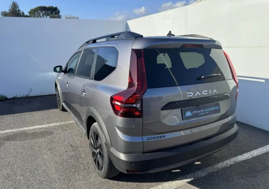 Vue 3/4 arrière gauche d'un Dacia Jogger gris schiste métallisé avec barres de toit et feux arrière LED distinctifs.