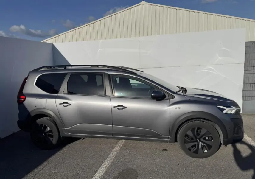 Vue de profil droit d'un Dacia Jogger gris schiste métallisé avec barres de toit et jantes noires.