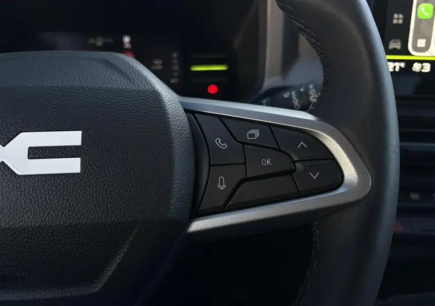 Gros plan sur les commandes multifonctions côté droit du volant noir du Dacia Duster 2025, avec écran tactile en arrière-plan.