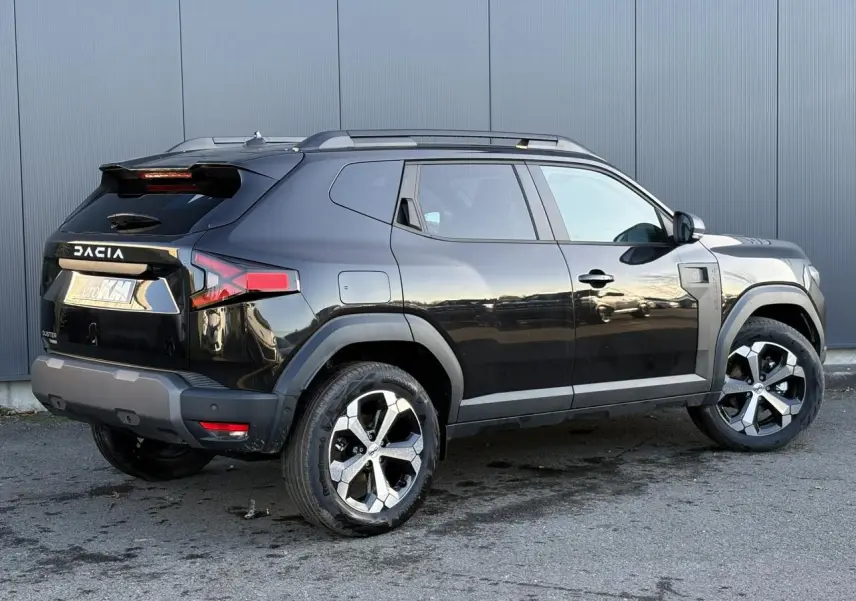 Vue 3/4 arrière droite du Dacia Duster 2025 noir nacré avec jantes alliage et barres de toit noires.