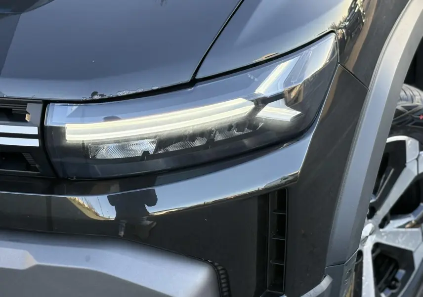 Gros plan sur le phare avant droit du Dacia Duster noir nacré avec jante alliage visible en arrière-plan.
