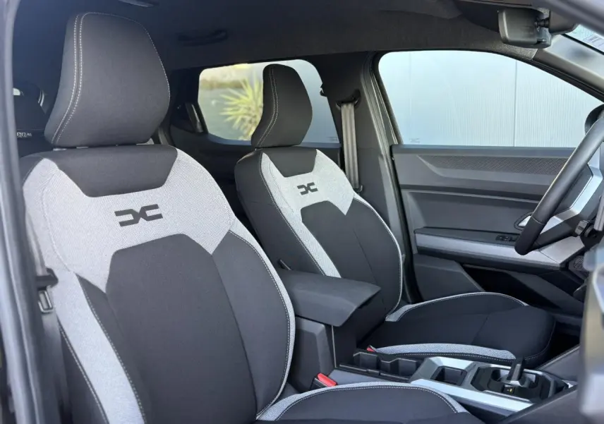 Vue intérieure côté droit du Dacia Duster 2025, sièges bi-ton gris et noir avec logo DC brodé.