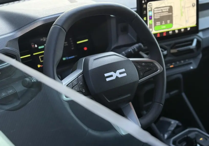 Vue rapprochée du volant noir du Dacia Duster 2025 avec tableau de bord digital et écran tactile central allumé.