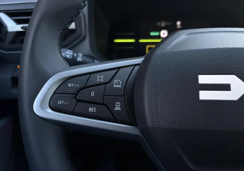 Gros plan sur le côté gauche du volant noir du Dacia Duster 2025 avec commandes de régulateur et assistance.