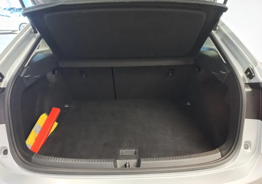 Coffre ouvert vu de l'arrière d'un Volkswagen Taigo 2025 argent métallisé avec triangle de signalisation et gilet jaune.