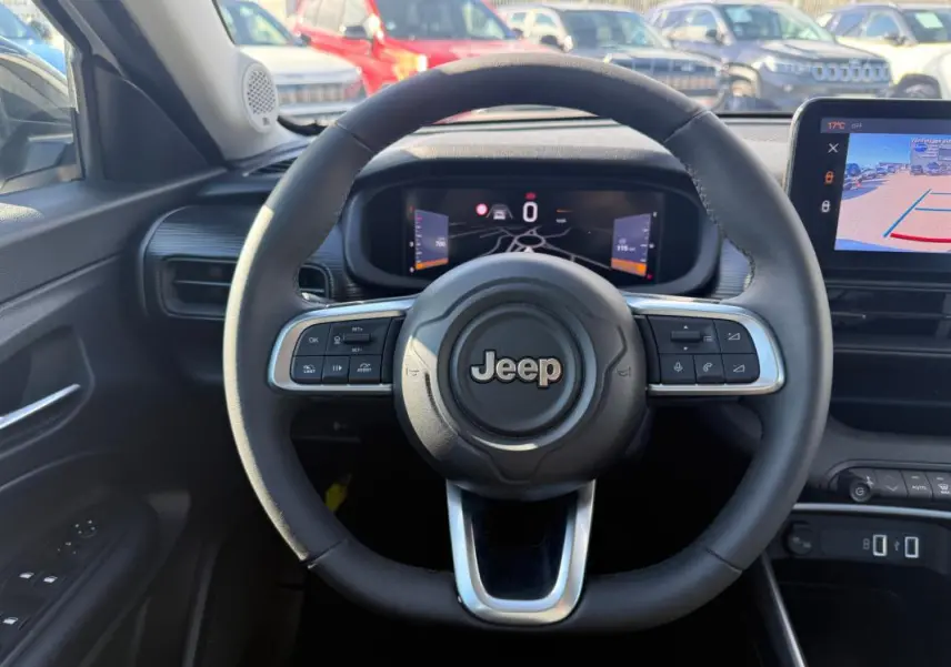 Vue intérieure centrée sur le volant Jeep noir avec tableau de bord numérique et écran de caméra de recul.