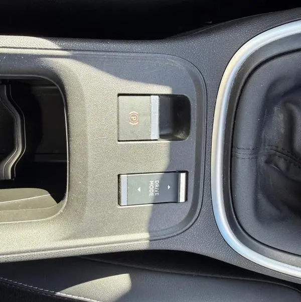 Vue rapprochée de la console centrale noire du Jeep Avenger 2025 avec frein à main électrique et bouton Drive Mode.