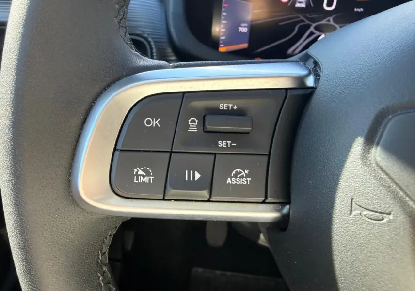 Gros plan sur les commandes du volant côté gauche du Jeep Avenger blanc, avec régulateur de vitesse et assistant de conduite.