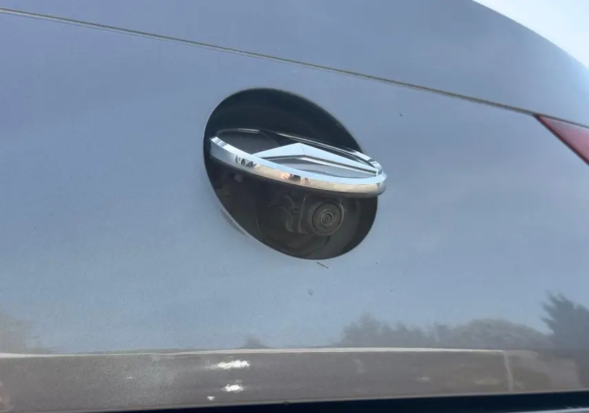 Gros plan sur la caméra de recul intégrée sous le logo chromé à l'arrière d'une Mercedes CLA 180 D gris montagne.