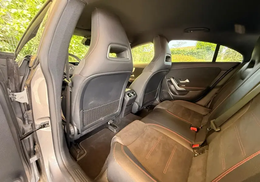 Vue intérieure arrière gauche de la Mercedes Classe CLA 180 D AMG Line gris montagne, sièges sport en cuir noir avec surpiqûres rouges.