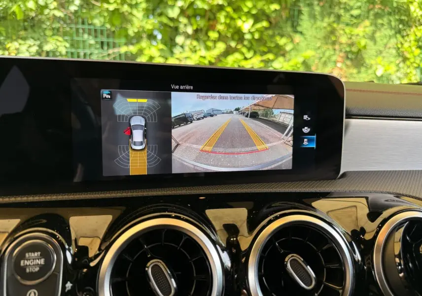 Écran central montrant la caméra de recul et les capteurs de stationnement du tableau de bord d'une Mercedes CLA gris montagne.