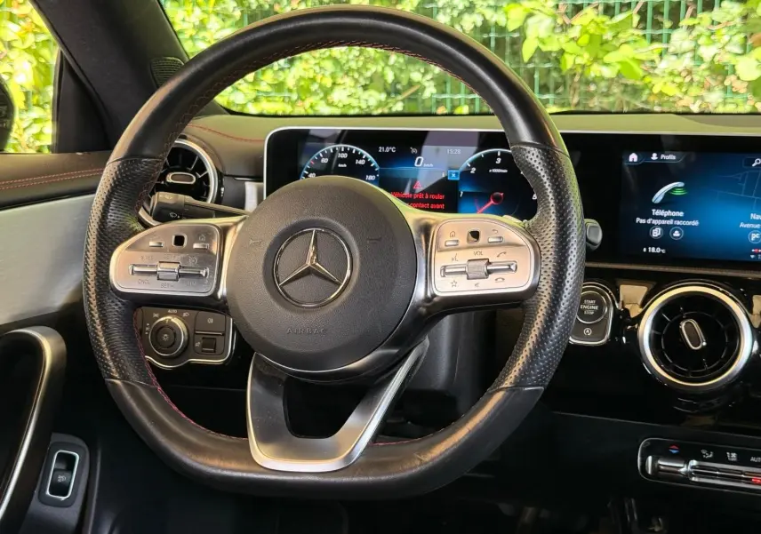 Vue intérieure centrée sur le volant cuir perforé et les écrans numériques du tableau de bord d'une Mercedes CLA gris montagne.