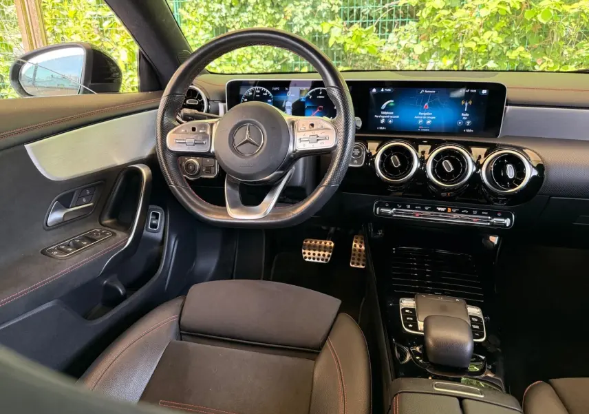 Vue intérieure avant du poste de conduite de la Mercedes Classe CLA 180 D AMG Line avec volant multifonction et écran digital large.