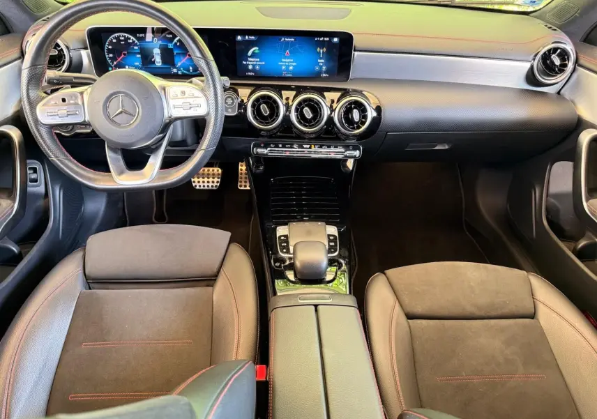 Vue intérieure avant de la Mercedes Classe CLA 180 D AMG Line 2019, tableau de bord moderne avec écran large et sièges en cuir noir à surpiqûres rouges.