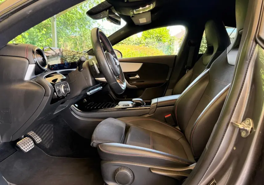 Vue intérieure côté conducteur de la Mercedes Classe CLA 180 D AMG Line 2019 avec sièges cuir noir et surpiqûres rouges.