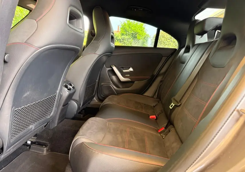 Vue intérieure arrière droite de la Mercedes Classe CLA 180 D AMG Line 2019 avec sièges en cuir noir et surpiqûres rouges.